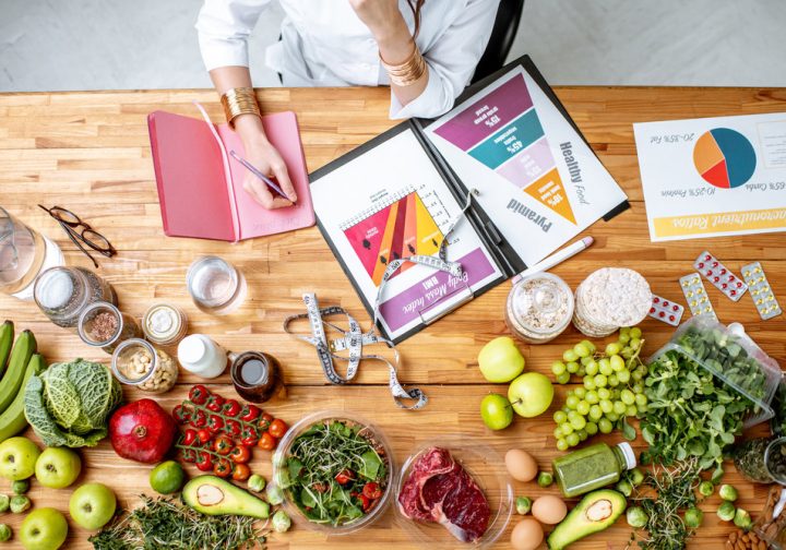 Dietitian writing diet plan, view from above on the table with different healthy products and drawings on the topic of healthy eating